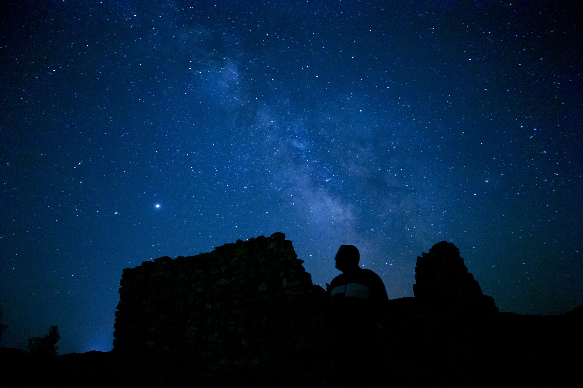 Magical view of silhouettes of a man sitting on the cliff stargazing the starry night sky